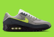 Nike Air Max 90 Neon, sneaker grise et noire avec Swoosh vert Neon, empiècements en mesh et unité Max Air visible au talon.