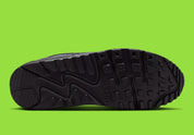 Nike Air Max 90 Neon, sneaker grise et noire avec Swoosh vert Neon, empiècements en mesh et unité Max Air visible au talon.