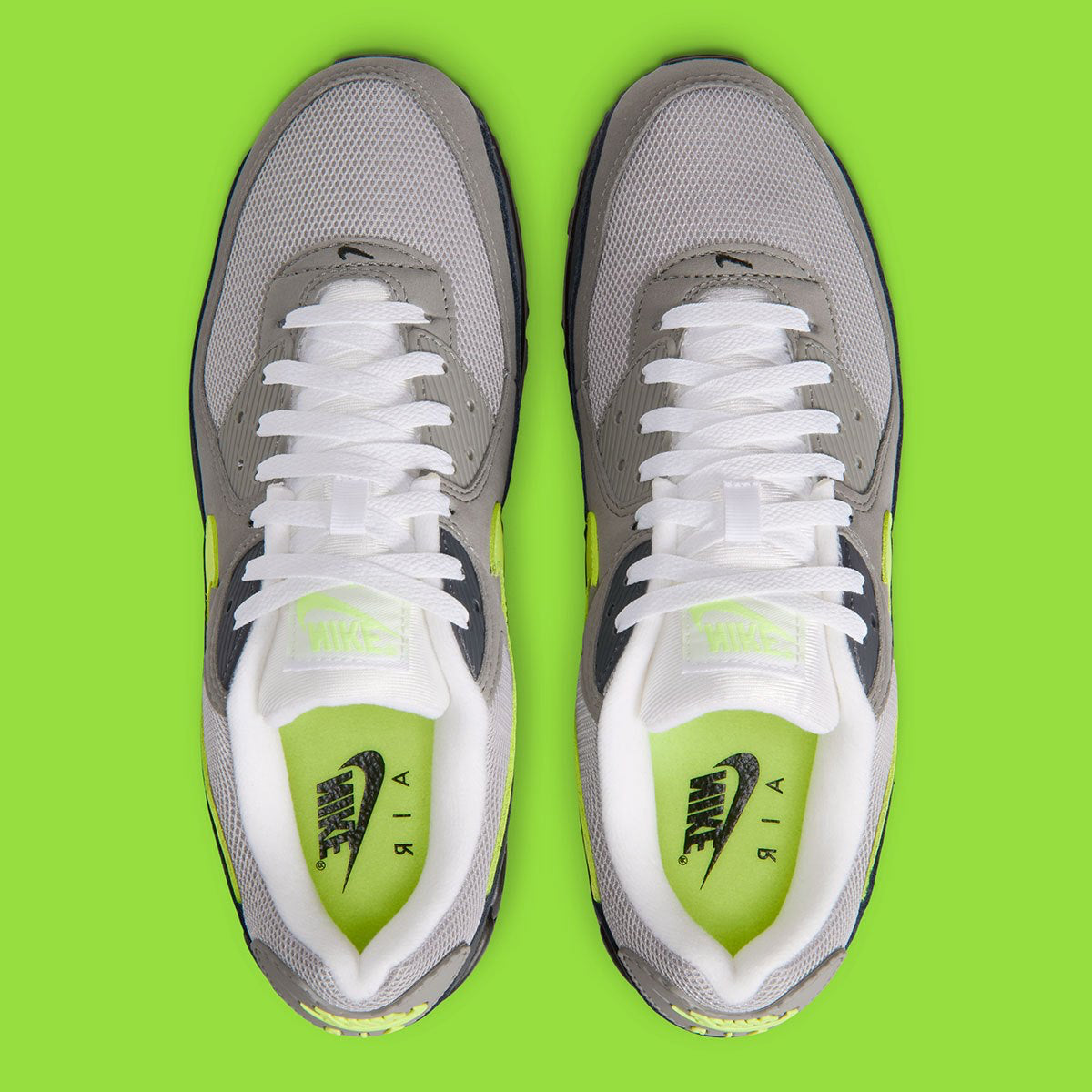 Nike Air Max 90 Neon, sneaker grise et noire avec Swoosh vert Neon, empiècements en mesh et unité Max Air visible au talon.