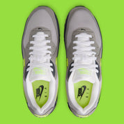 Nike Air Max 90 Neon, sneaker grise et noire avec Swoosh vert Neon, empiècements en mesh et unité Max Air visible au talon.