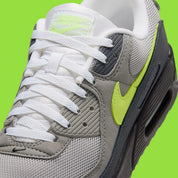 Nike Air Max 90 Neon, sneaker grise et noire avec Swoosh vert Neon, empiècements en mesh et unité Max Air visible au talon.