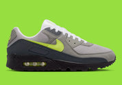 Nike Air Max 90 Neon, sneaker grise et noire avec Swoosh vert Neon, empiècements en mesh et unité Max Air visible au talon.