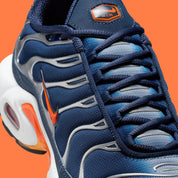 Vue zoomée sur les détails latéraux de la Nike Air Max Plus Syracuse bleu marine avec cage TPU gris argenté, Swoosh orange et unités Tuned Air visibles.