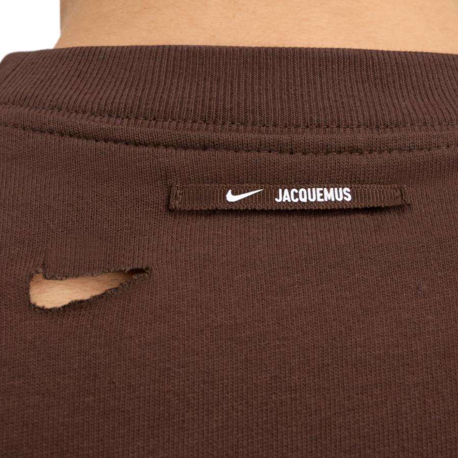 Vue zoomée sur les détails du Jacquemus x Nike Le Swoosh T-shirt Brown à manches courtes, coloris brun, col rond et détail Swoosh Nike revisité dans l'univers minimaliste de Jacquemus.