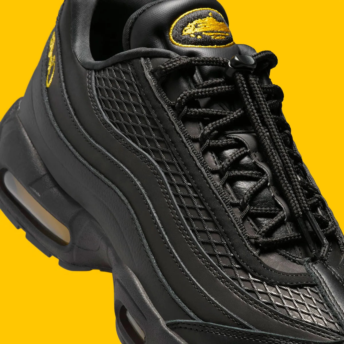 Vue zoomée sur les détails latéraux de la Nike Air Max 95 Corteiz Honey Black noire en cuir et mesh diamant avec détails Corteiz, logo Alcatraz et unités Air Max Tour Yellow.