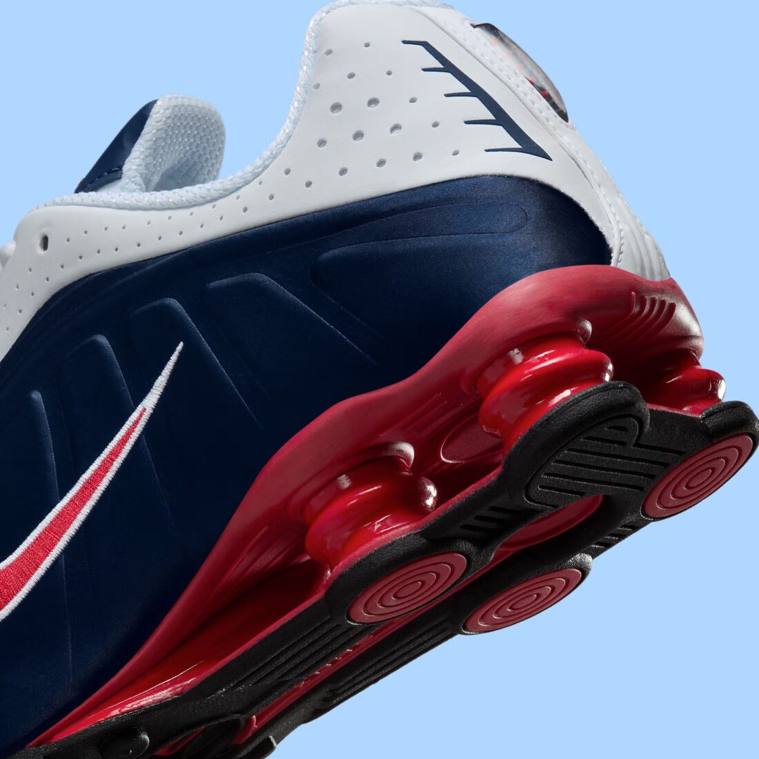 Nike Shox R4 USA 2025 avec tige en cuir synthétique blanc et bleu marine, détails Metallic Silver et Gym Red, amorti Nike Shox à quatre colonnes et semelle extérieure en caoutchouc.