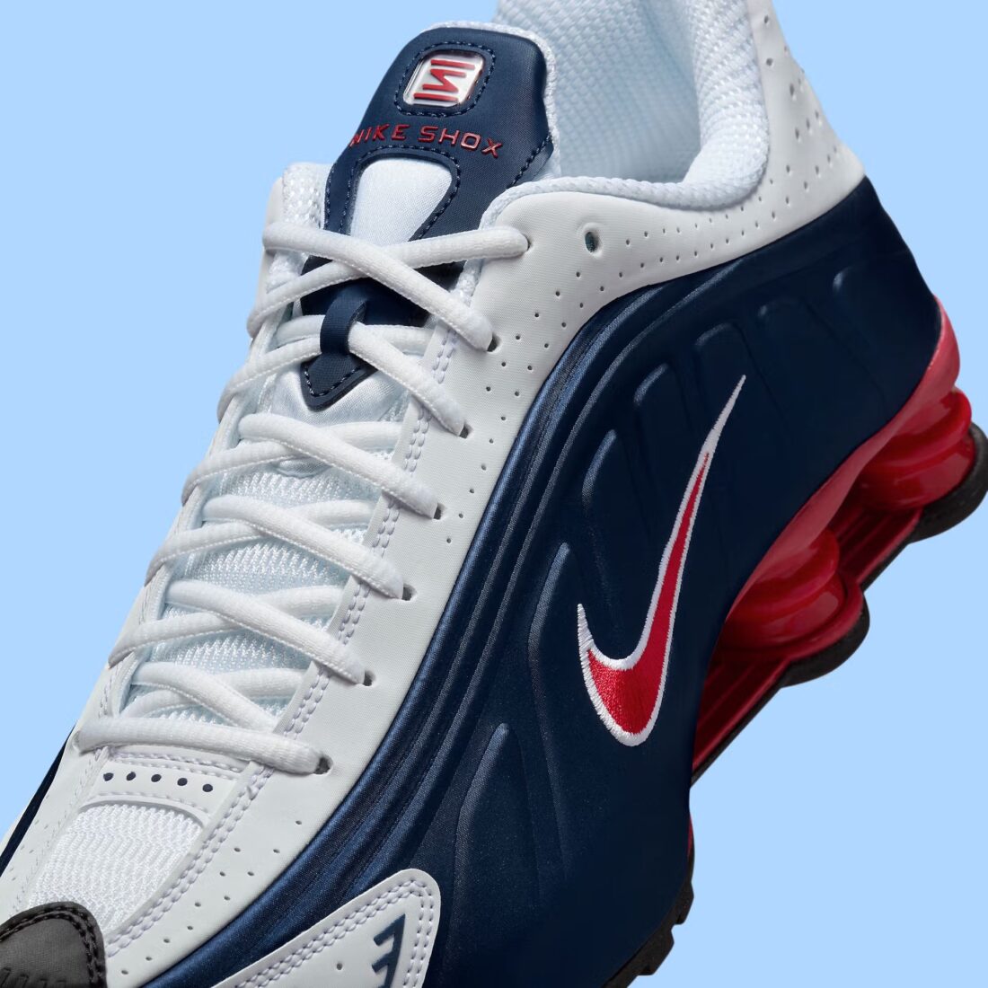 Nike Shox R4 USA 2025 avec tige en cuir synthétique blanc et bleu marine, détails Metallic Silver et Gym Red, amorti Nike Shox à quatre colonnes et semelle extérieure en caoutchouc.