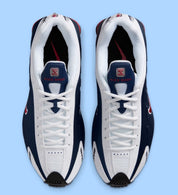 Nike Shox R4 USA 2025 avec tige en cuir synthétique blanc et bleu marine, détails Metallic Silver et Gym Red, amorti Nike Shox à quatre colonnes et semelle extérieure en caoutchouc.