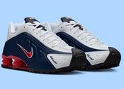 Nike Shox R4 USA 2025 avec tige en cuir synthétique blanc et bleu marine, détails Metallic Silver et Gym Red, amorti Nike Shox à quatre colonnes et semelle extérieure en caoutchouc.