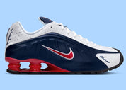 Nike Shox R4 USA 2025 avec tige en cuir synthétique blanc et bleu marine, détails Metallic Silver et Gym Red, amorti Nike Shox à quatre colonnes et semelle extérieure en caoutchouc.