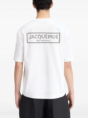 TEE SHIRT JACQUEMUS BLANC AVEC UN LOGO "J" EN FORME DE POISSON SUR LE COEUR ET UN GROS CADRE INSCRIT JACQUEMUS AU DOS DU TEE-SHIRT