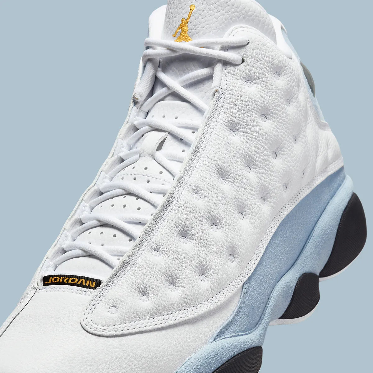 Vue zoomée sur les détails latéraux de la Air Jordan 13 Retro Blue Grey 414571-170 en cuir blanc avec panneaux Blue Grey, détails noirs, accents Yellow Ochre et hologramme vert.