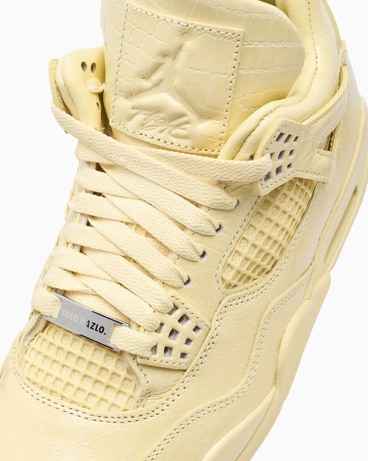 Vue zoomée sur la languette de la Air Jordan 4 Retro J Balvin Lemonade IW2872-700 en jaune Lemonade avec textures effet crocodile, détails multicolores et smiley J Balvin au talon.