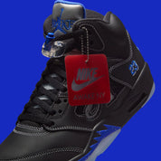 Vue latérale de la Air Jordan 5 Retro Awake NY Black DV4982-004, sneaker noire en cuir avec détails Racer Blue, languette argentée et logos Awake NY avec son étiquette. 