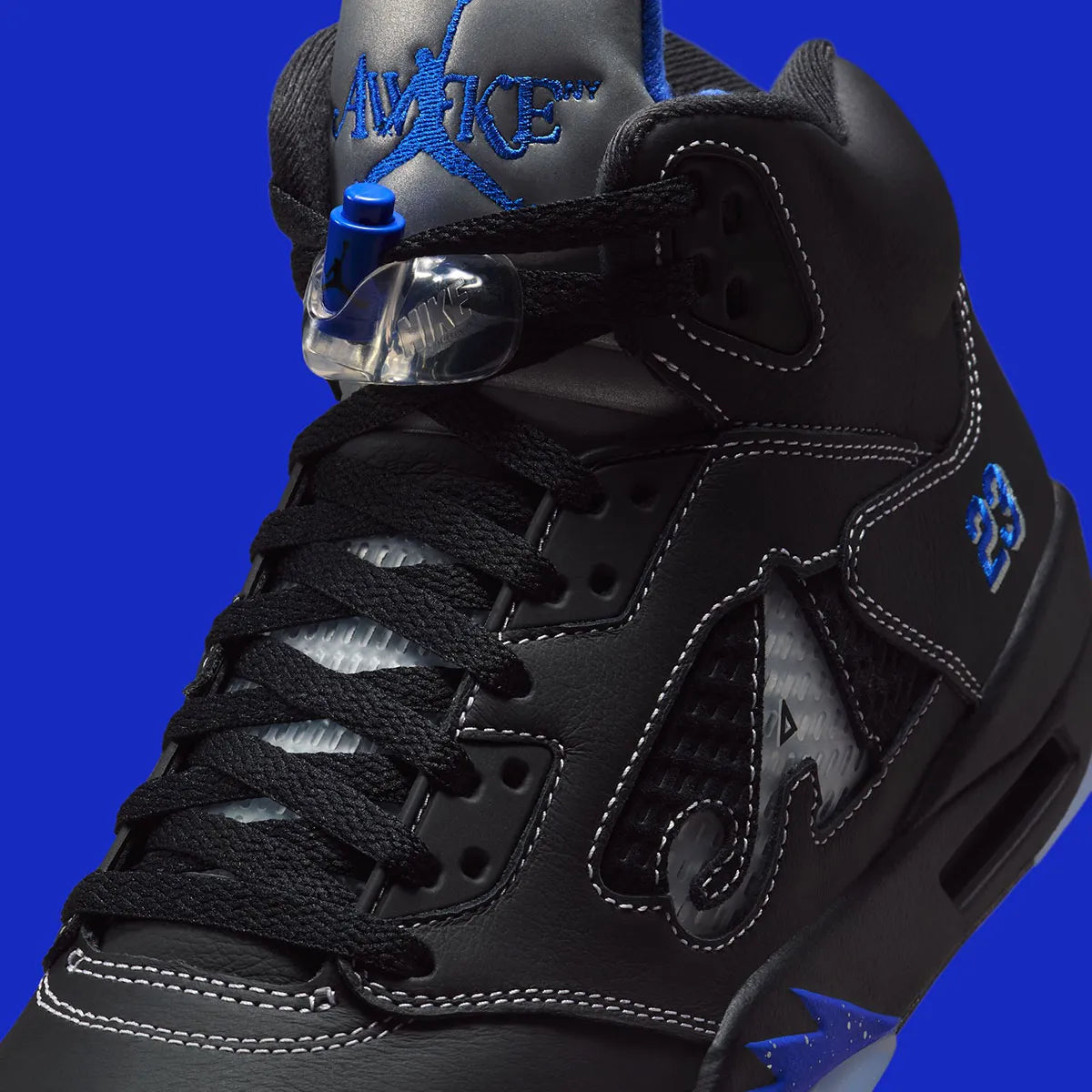 Vue zoomée sur les détails latéraux de la Air Jordan 5 Retro Awake NY Black DV4982-004, sneaker noire en cuir avec détails Racer Blue, languette argentée et logos Awake NY.