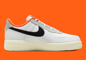 Nike Air Force 1 Low 07 Hoops, sneaker blanche et noire avec détails orange, semelle crème et graphisme basketball au talon vue de profil. 