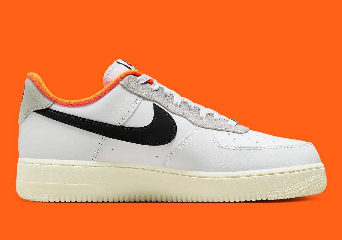Nike Air Force 1 Low 07 Hoops, sneaker blanche et noire avec détails orange, semelle crème et graphisme basketball au talon vue de profil. 