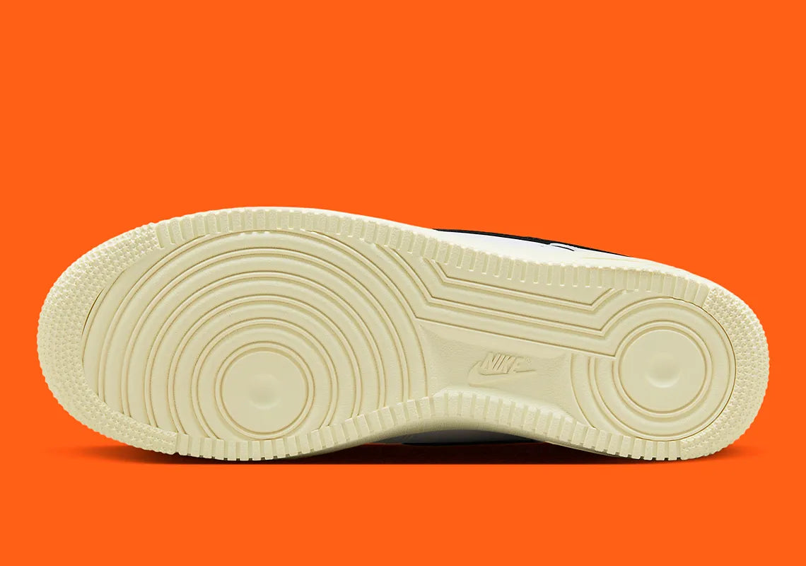 Nike Air Force 1 Low 07 Hoops, sneaker blanche et noire avec détails orange, semelle crème et graphisme basketball au talon vue de profil. 
