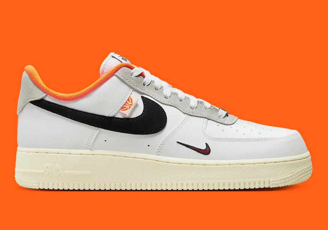 Nike Air Force 1 Low 07 Hoops, sneaker blanche et noire avec détails orange, semelle crème et graphisme basketball au talon vue de profil. 