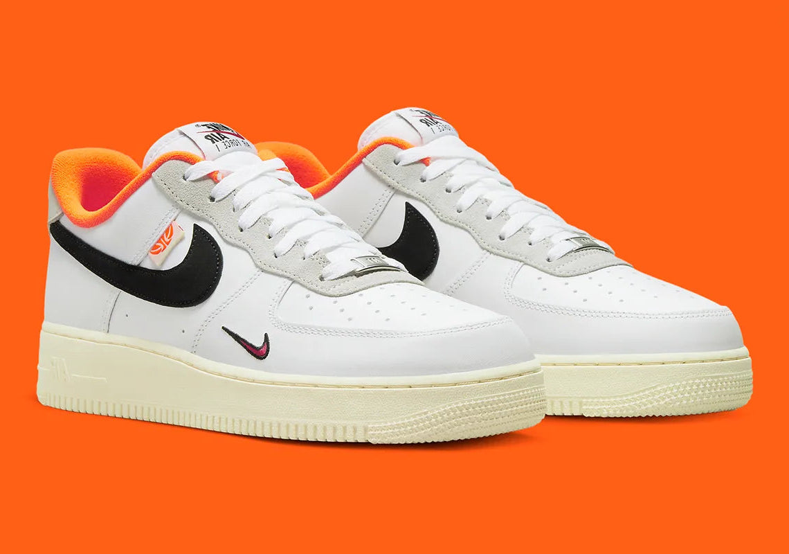 Nike Air Force 1 Low 07 Hoops, sneaker blanche et noire avec détails orange, semelle crème et graphisme basketball au talon vue de profil. 