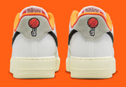 Nike Air Force 1 Low 07 Hoops, sneaker blanche et noire avec détails orange, semelle crème et graphisme basketball au talon vue de profil. 