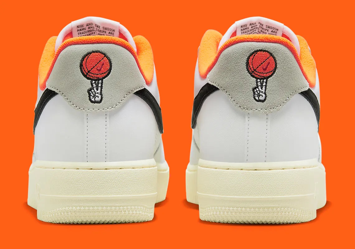 Nike Air Force 1 Low 07 Hoops, sneaker blanche et noire avec détails orange, semelle crème et graphisme basketball au talon vue de profil. 