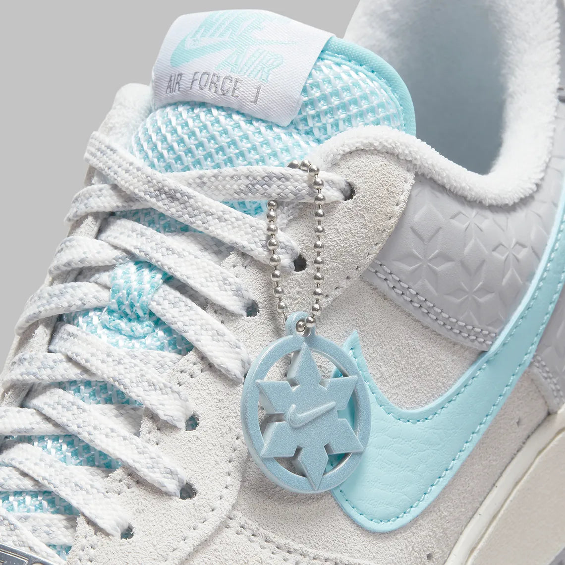 Nike Air Force 1 Low Snowflake DQ0790-001, sneaker Nike Air Force 1 grise en suède avec Swoosh bleu clair et motifs flocons de neige embossés.