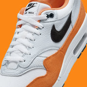 Nike Air Max 1 Monarch FN6952-101 en mesh blanc, cuir gris et suède orange Monarch avec Swoosh noir et unité Air visible.