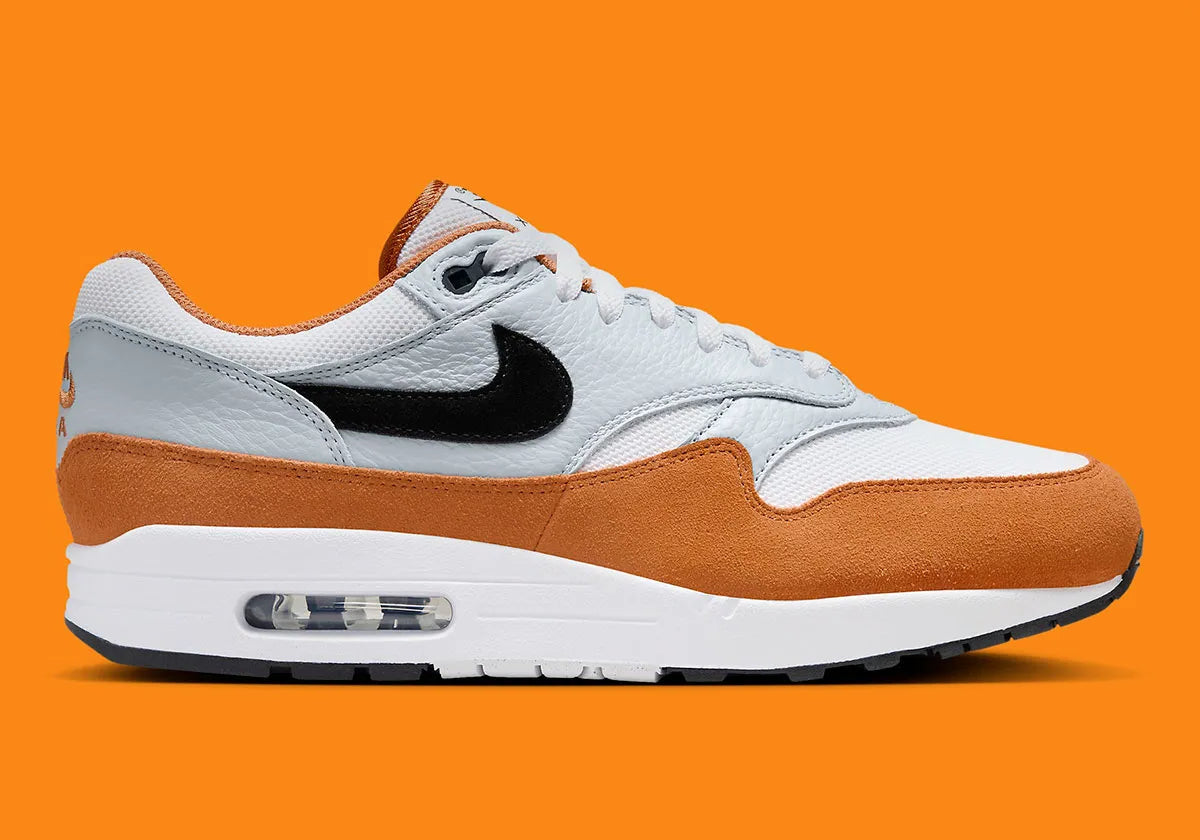 Nike Air Max 1 Monarch FN6952-101 en mesh blanc, cuir gris et suède orange Monarch avec Swoosh noir et unité Air visible.