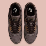 Nike Air Max 90 Shadow Brown, sneaker Nike marron avec empeigne multi-matières, Swoosh latéral et unité Air visible au talon.