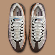 Nike Air Max 95 Unearthed beige et marron avec panneaux multicouches Summit White, Cacao Wow et Velvet Brown et unités Air bleues visibles.