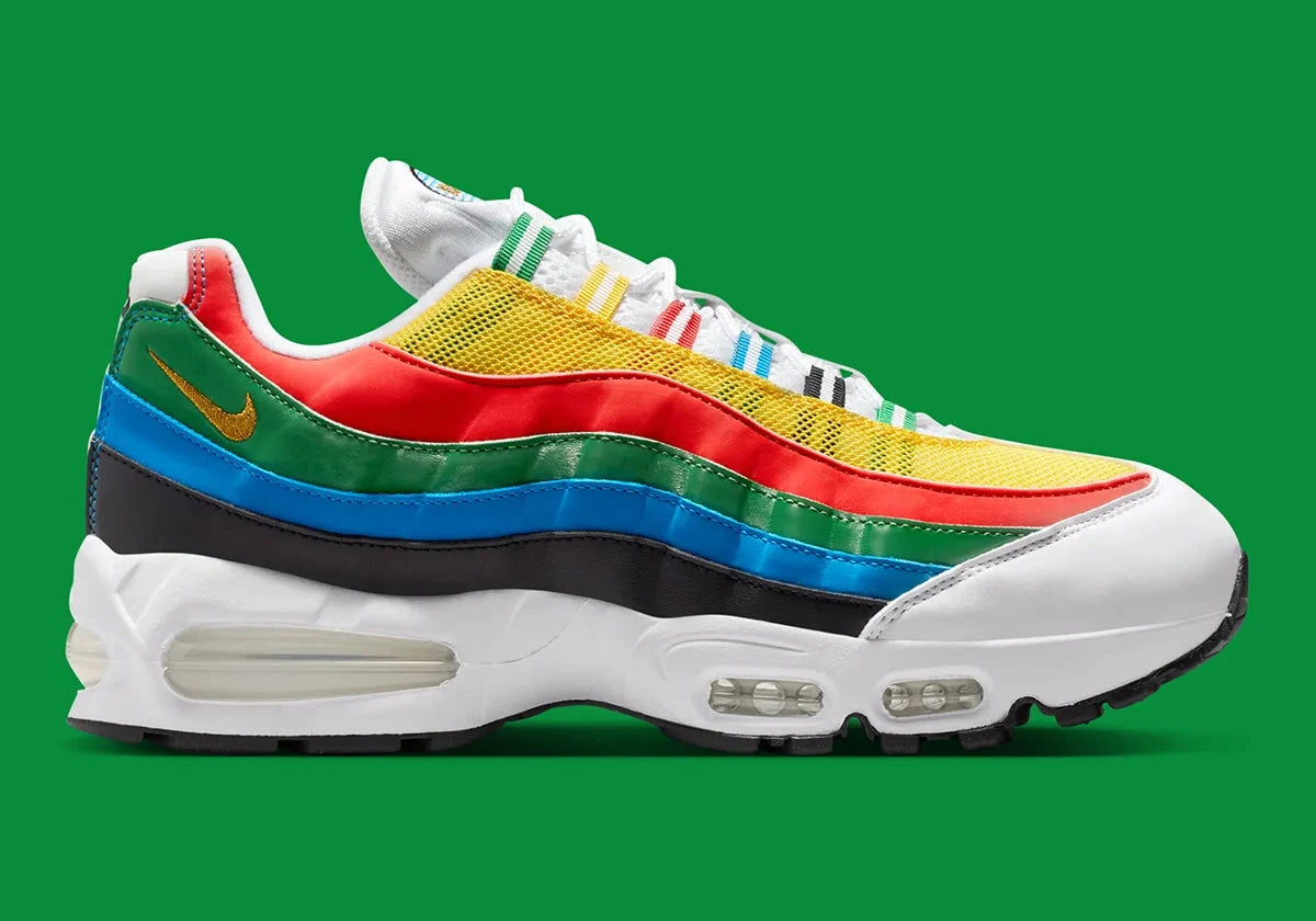 Nike Air Max 95 Olympic 2026 avec tige en mesh, cuir synthétique et suède blanc et bleu, détails Metallic Gold, unités Max Air visibles et semelle extérieure en caoutchouc vue de profil. 