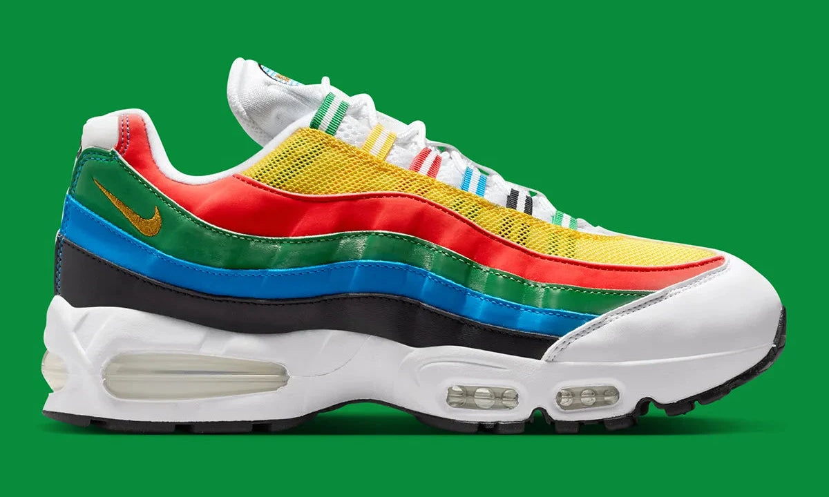 Nike Air Max 95 Olympic 2026 avec tige en mesh, cuir synthétique et suède blanc et bleu, détails Metallic Gold, unités Max Air visibles et semelle extérieure en caoutchouc vue de profil. 