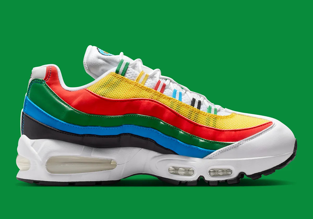 Nike Air Max 95 Olympic 2026 avec tige en mesh, cuir synthétique et suède blanc et bleu, détails Metallic Gold, unités Max Air visibles et semelle extérieure en caoutchouc vue de profil. 