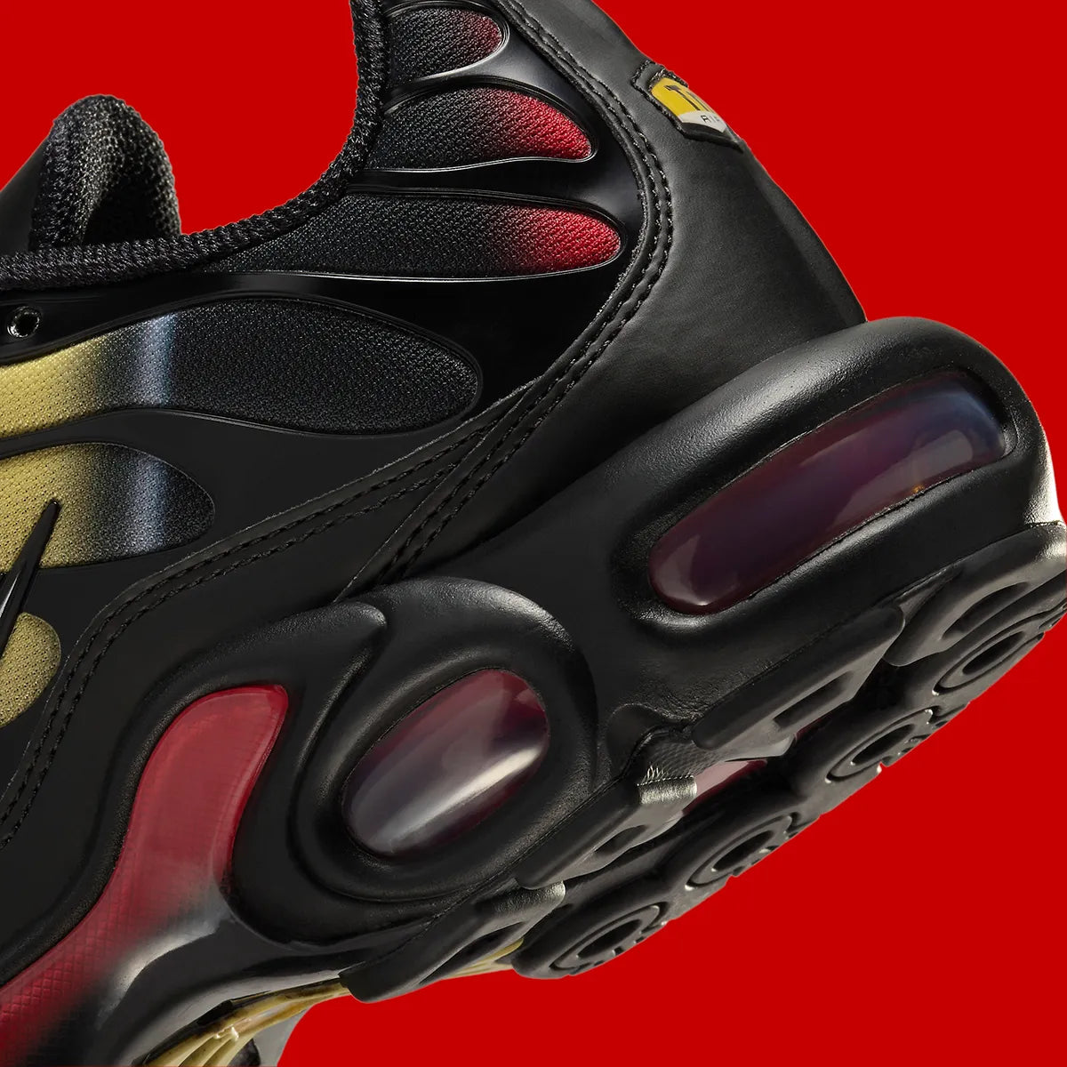 Image de la Nike Air Max Plus Orbit, sneaker en mesh noir avec superpositions métalliques, accents Saturn Gold et Light Crimson, unités Tuned Air visibles sur semelle blanche, style TN revisité cosmos. Vue zoomer arrière 
