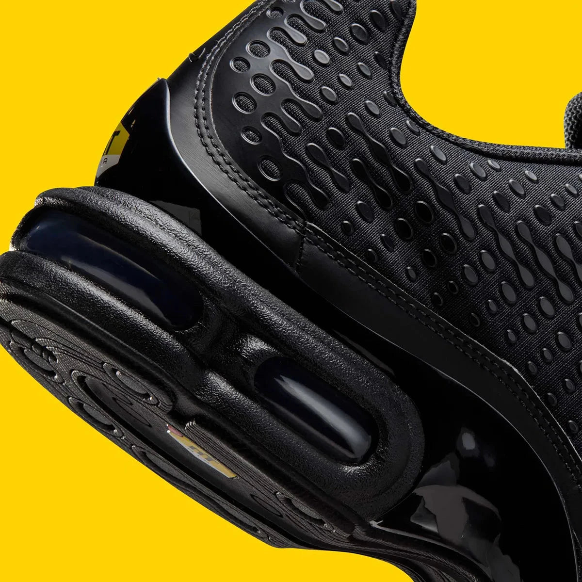 Vue zoomée sur les détails arrières de la Nike Air Max Plus 7 Black noire et anthracite avec tige en mesh, renforts ondulés et unités Nike Air visibles. 