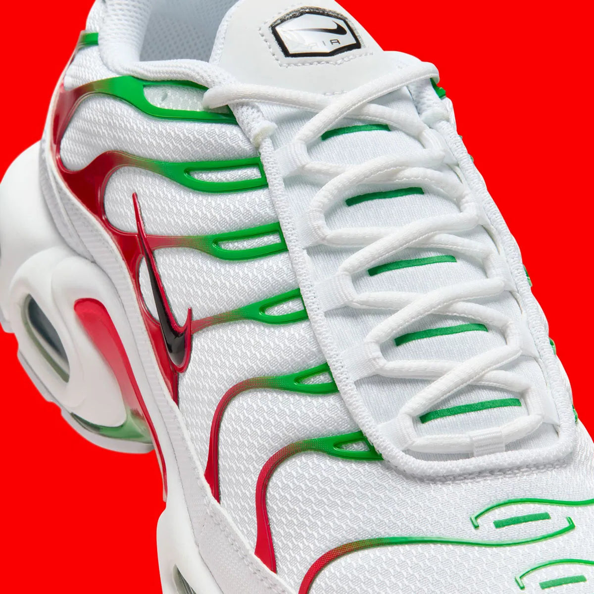 Vue zoomée sur les détails latéraux de la Nike Air Max Plus Italy blanche avec renforts TPU verts et rouges, Swoosh noir et unités Tuned Air visibles. 