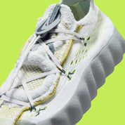 Nike Mind 002 Flyknit White Dark Grey Volt avec tige en Flyknit blanc et gris foncé, accents Volt fluorescents et semelle moderne offrant confort et adhérence.