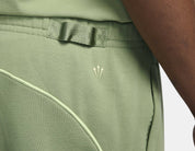 Nike x NOCTA Fleece CS Sweatpant Oil Green/Light Liquid Lime, pantalon fleece vert avec coupe ample, poches zippées et détails réfléchissants NOCTA.
