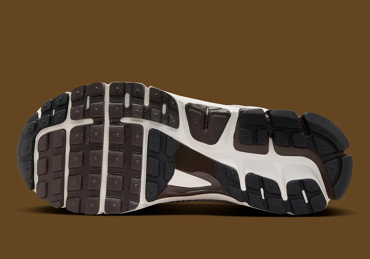 Image de la Nike Zoom Vomero 5 Phantom / Light Iron Ore, sneaker gris clair et blanc cassé en mesh et cuir, superpositions gris acier, semelle noire à amorti Zoom Air visible.