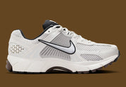 Image de la Nike Zoom Vomero 5 Phantom / Light Iron Ore, sneaker gris clair et blanc cassé en mesh et cuir, superpositions gris acier, semelle noire à amorti Zoom Air visible.