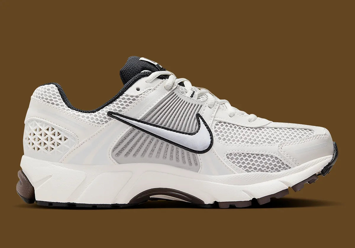 Image de la Nike Zoom Vomero 5 Phantom / Light Iron Ore, sneaker gris clair et blanc cassé en mesh et cuir, superpositions gris acier, semelle noire à amorti Zoom Air visible.