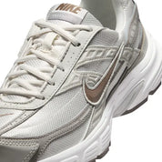 Vue zoomée sur les détails latéraux de la Nike Initiator Phantom Light Bone Sail Mink Brown IB4339-001 avec tige crème et beige, détails bruns et silhouette rétro-running multicouche. 