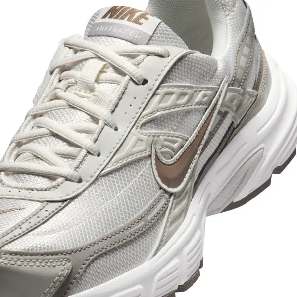 Vue zoomée sur les détails latéraux de la Nike Initiator Phantom Light Bone Sail Mink Brown IB4339-001 avec tige crème et beige, détails bruns et silhouette rétro-running multicouche. 