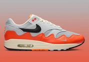 Sneakers Nike Air Max 1 Patta Waves Hyper Crimson Pure Platinum en mesh gris et cuir avec garde-boue ondulé orange et unité Air visible.