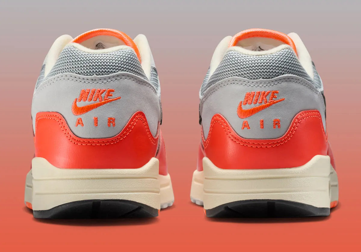 Sneakers Nike Air Max 1 Patta Waves Hyper Crimson Pure Platinum en mesh gris et cuir avec garde-boue ondulé orange et unité Air visible.