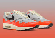 Sneakers Nike Air Max 1 Patta Waves Hyper Crimson Pure Platinum en mesh gris et cuir avec garde-boue ondulé orange et unité Air visible.