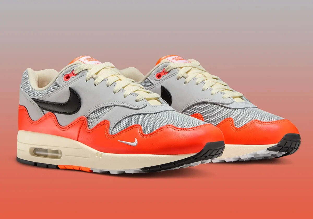 Sneakers Nike Air Max 1 Patta Waves Hyper Crimson Pure Platinum en mesh gris et cuir avec garde-boue ondulé orange et unité Air visible.
