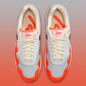Sneakers Nike Air Max 1 Patta Waves Hyper Crimson Pure Platinum en mesh gris et cuir avec garde-boue ondulé orange et unité Air visible.