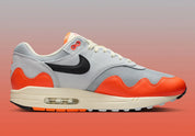 Sneakers Nike Air Max 1 Patta Waves Hyper Crimson Pure Platinum en mesh gris et cuir avec garde-boue ondulé orange et unité Air visible.